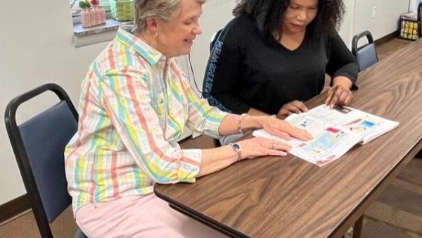 a person sitting at a table with a person looking at a piece of paper